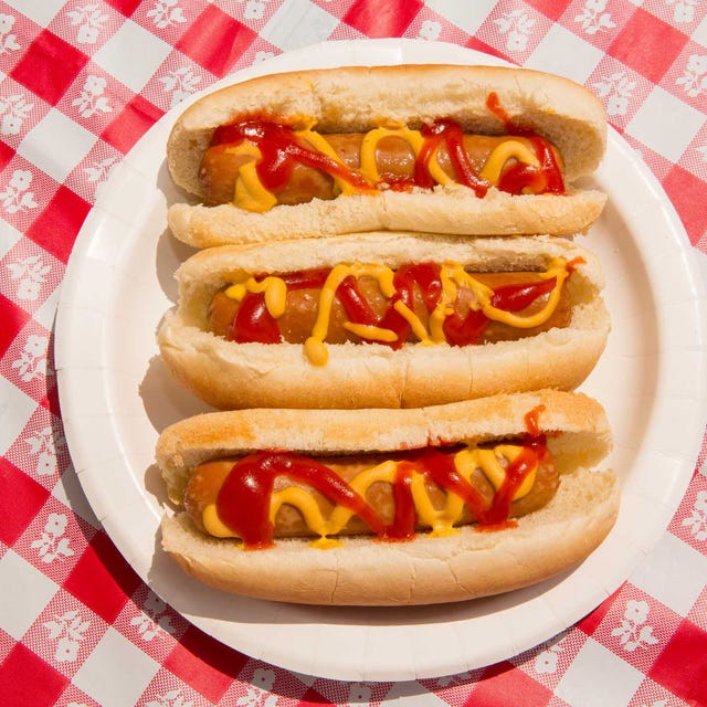 america, fourth of july foods hot dogs indulgence and overeating concept for unhealthy eating of junk food, carefree summer picnic, independence day or memorial day backyard bbq july 4th bbq food, no people foods featured are hot dogs with ketchup and mustard and pickles there are patriotic american flag toothpicks as decoration in the festive food paper plates and disposable plastic cups are also on the checkered tablecloth shot during sunny day outdoors on vacation part of a series