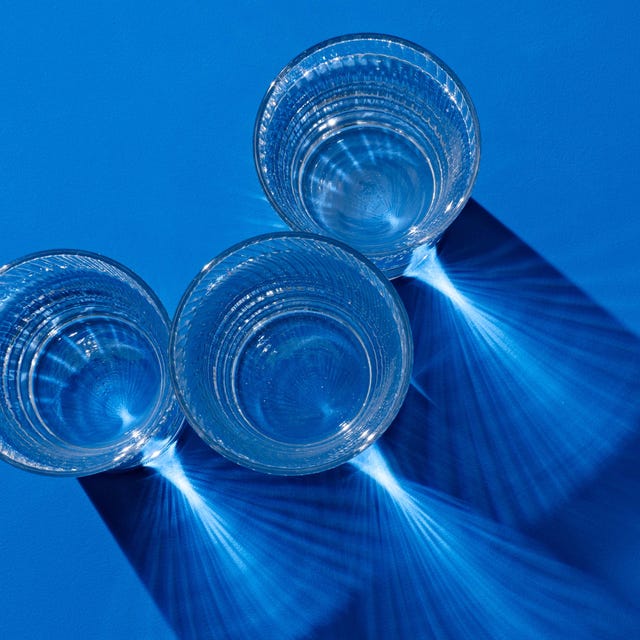 glasses of clear protein drinks with long shadow on deep blue colored background view