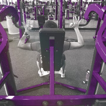 Gym scene featuring an individual exercising on a machine with purple-colored equipment.
