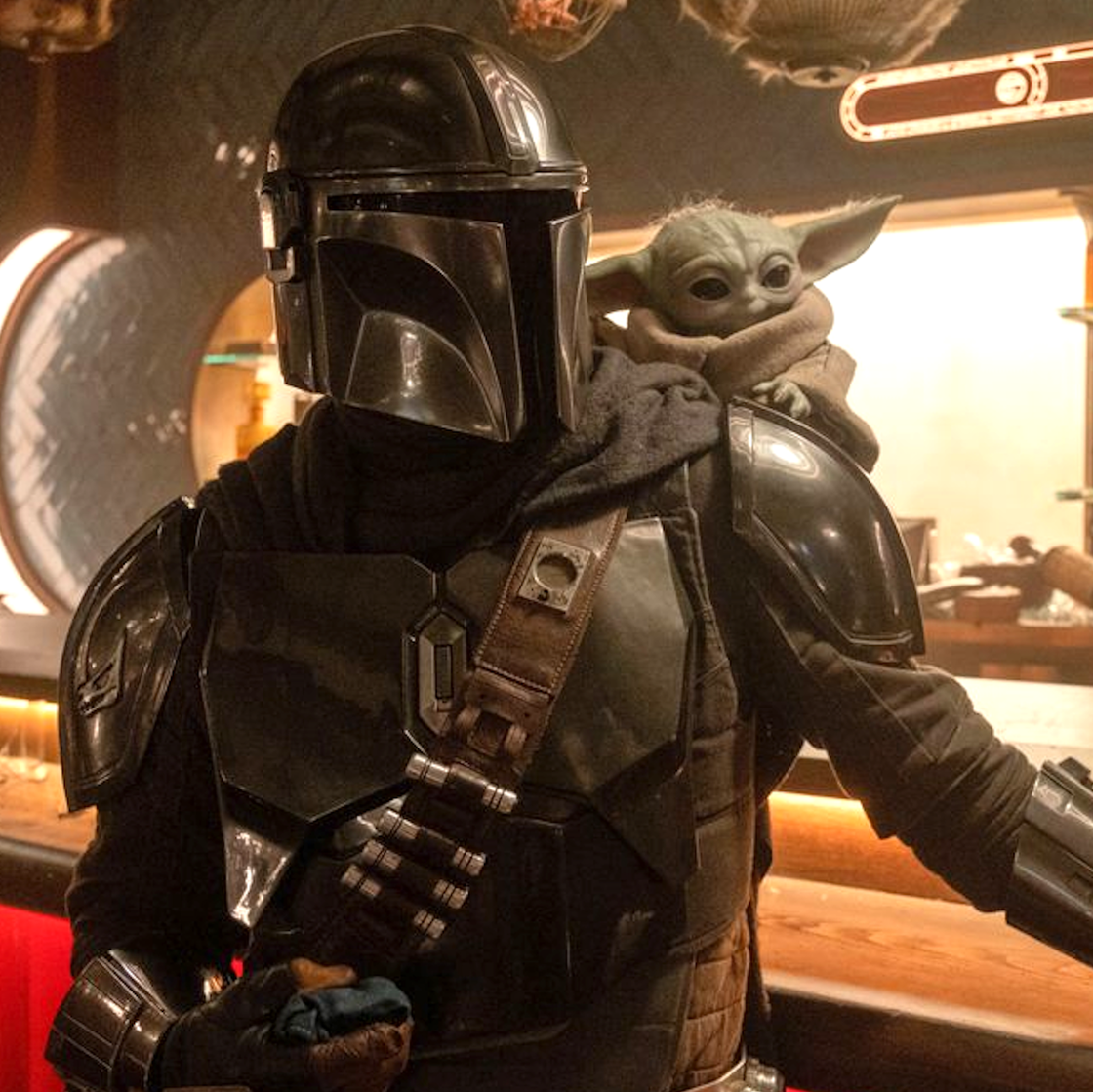 The Mandalorian holding Grogu in a protective stance.
