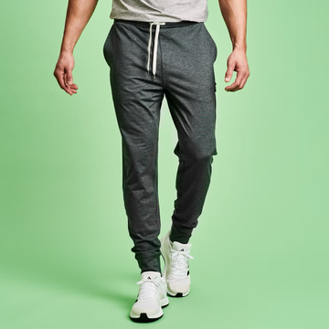 Male model wearing gray joggers and white sneakers against a green background.
